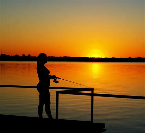 A Woman Fishing At Sunset With The Sun Setting Over The Water In The