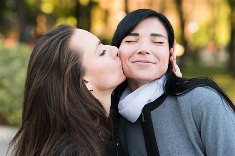 Premium Photo Happy Lesbian Caucasian Couple Kissing On The Cheek Standing In The Park In