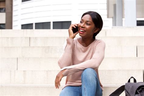 Happy Young Black Woman Sitting Outside And Talking On Mobile Phone