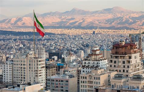 Aerial View Of Tehran Skyline At Sunset With Large Iran Flag Waving In