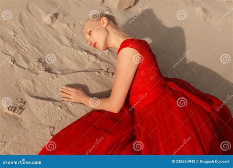 Beautiful Blonde Model In A Elegant Red Dress Lies On The Sand