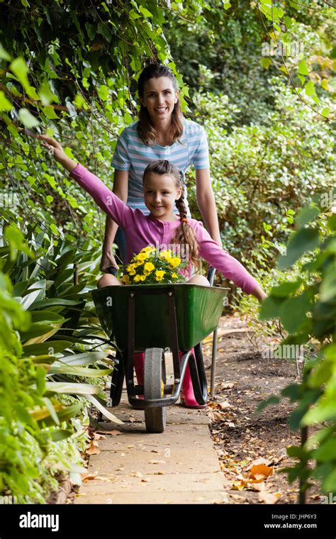 Woman Pushing Girl Sitting With Outstretched In Wheelbarrow On Footpath