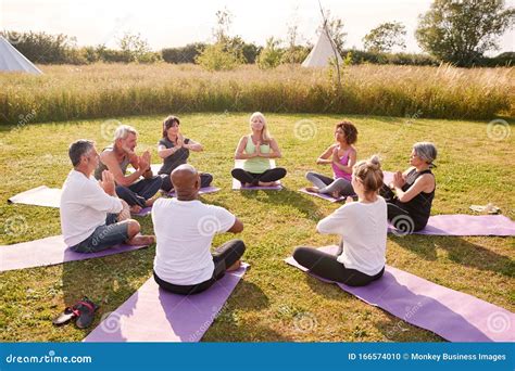 Group Of Mature Men And Women In Class At Outdoor Yoga Retreat Sitting Circle Meditating Stock