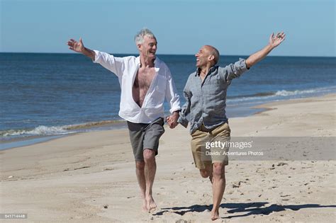 Senior Gay Couple Holding Hands And Joyfully Running Together On Beach