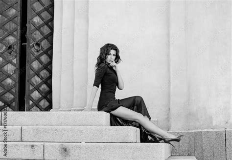 An Attractive Sexy Slender Brunette In A Long Black Dress With A Slit Sitting On The Steps Of A