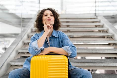 Pensive Young Woman Sitting With Suitcase On Stairs In Airport Stock
