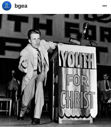 an old photo of a man standing in front of a youth for christ sign and speaking into a microphone