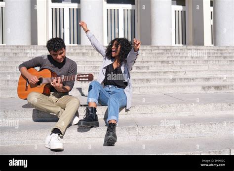 A Young Latin Couple Playing The Guitar And Singing Sitting On Stairs