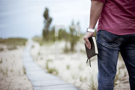 A Man Holding A Bible Walking On A Boardwalk — Photo — Lightstock