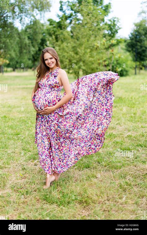 Beautiful Pregnant Woman Walking Barefoot In The Park In Long Colorful Dress With Flying Fabric