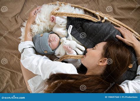 Young Happy Mother And A Sleeping Baby In A Wicker Cradle In A Warm