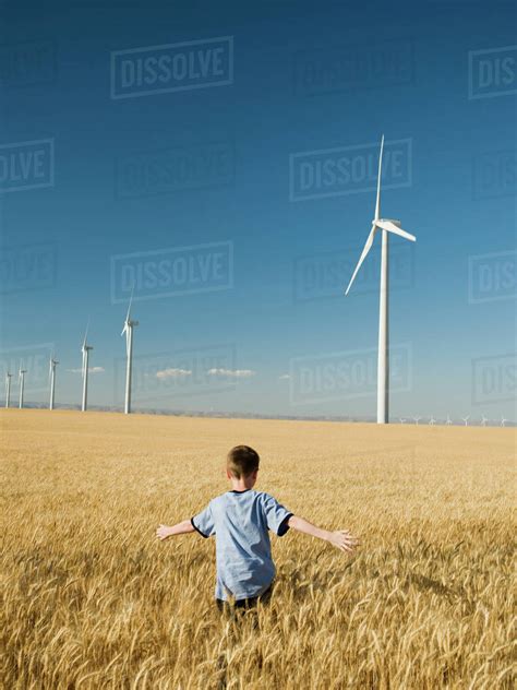 Boy Running Through Field On Wind Farm Stock Photo Dissolve