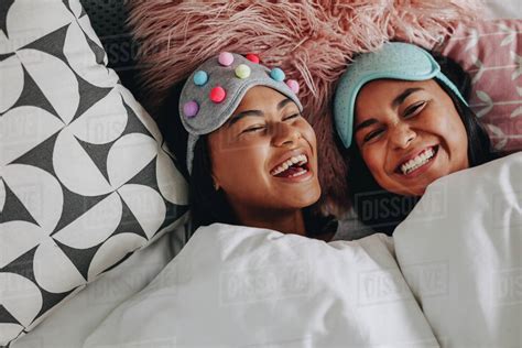Top View Of Two Teenage Girls Laughing With Eyes Closed Lying On Bed Having A Sleepover Teenage