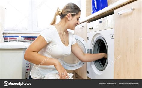 Portrait Of Young Smiling Woman Loading Clothes In Washing Machine