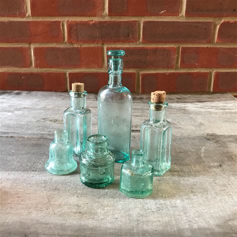 Four Glass Bottles Sitting On Top Of A Wooden Table Next To A Brick Wall