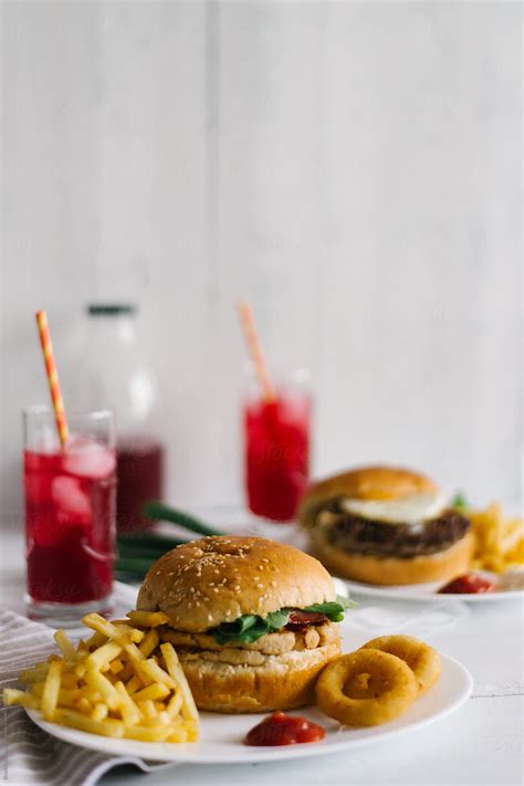 Burgers With Fries And Onion Rings Served On The Table By Stocksy