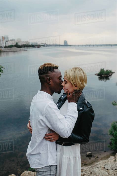 Interracial Couple Kisses And Hugs Against Background Of River And City