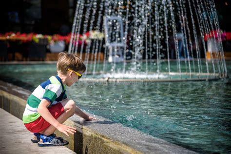 Little Boy Plays In The Square Near Pool With Water Jets In The