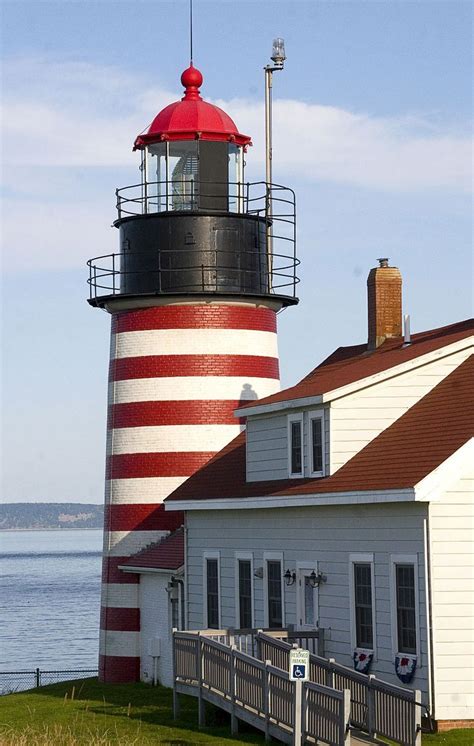 A Red And White Striped Lighthouse Next To A Body Of Water On A Sunny Day