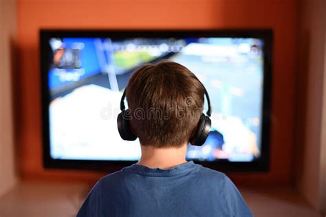Child With Headphones On His Back In Front Of The Tv Stock Image