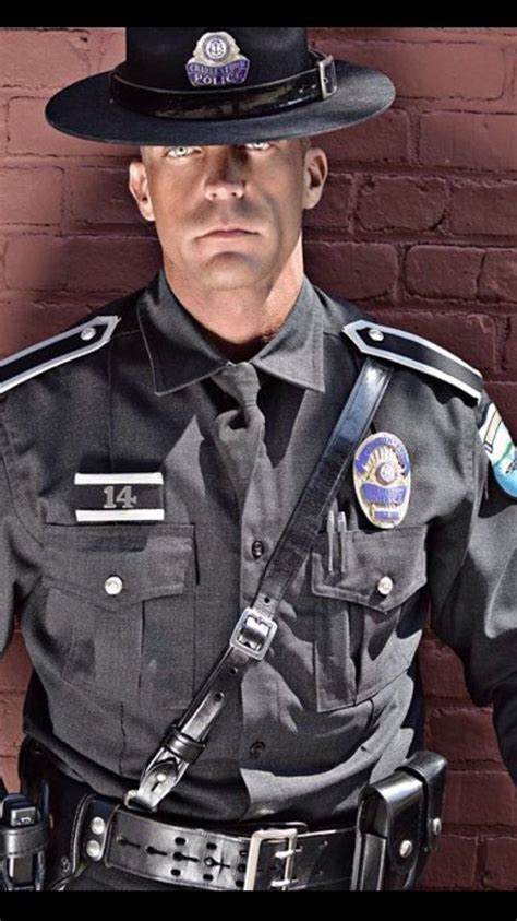 A Police Officer Is Standing In Front Of A Brick Wall With His Hands On