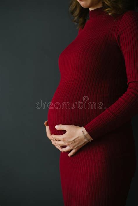 a pregnant woman in a knitted burgundy dress holds her hands on her stomach beautiful and happy