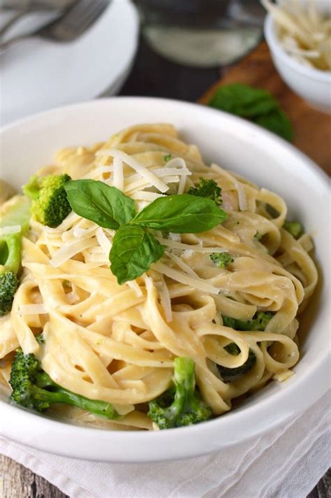 A White Bowl Filled With Pasta And Broccoli On Top Of A Wooden Table