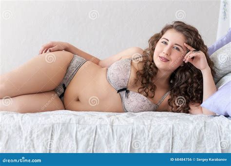 Plus Size Smiling Female In Underwear Lying On Its Side On Bed Stock
