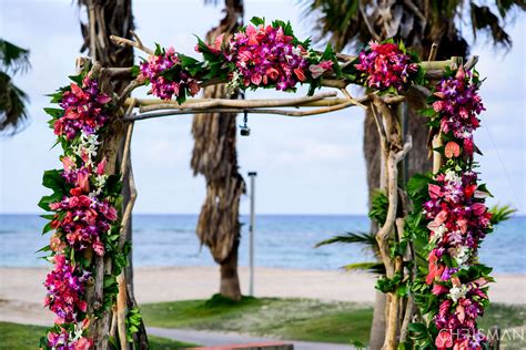 An Arch Made Out Of Branches With Flowers On The Beach In Front Of Palm