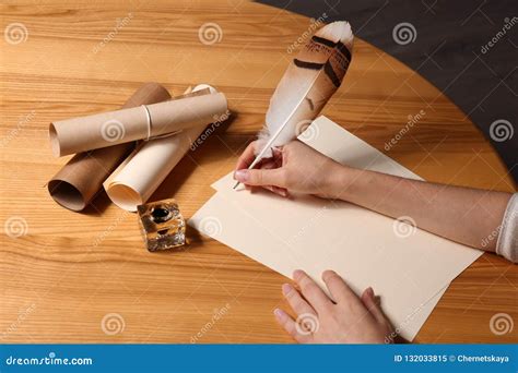 Woman Using Feather Pen To Write With Ink On Parchment At Wooden Table