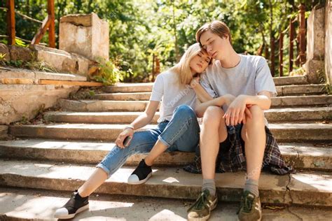 Young Beautiful Couple Sitting On Stairs In Park And Dreamily Closing