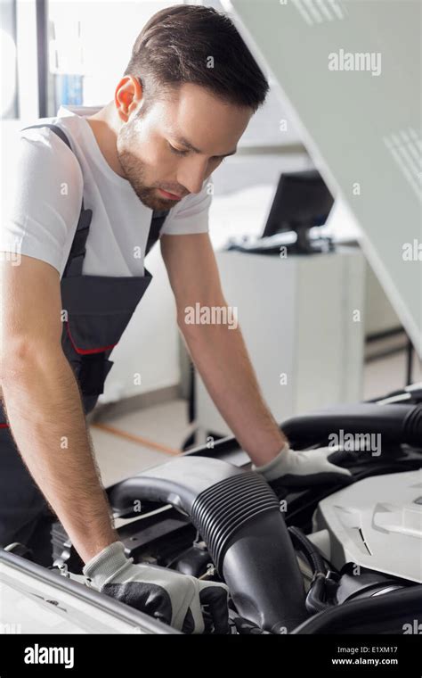 Full Length Side View Of Male Mechanic Examining Car Engine In Repair