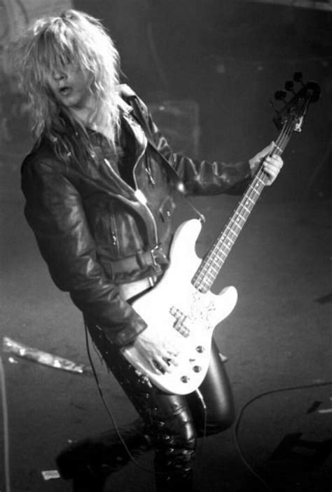 A Man With Long Hair And Leather Jacket Playing Guitar In Front Of