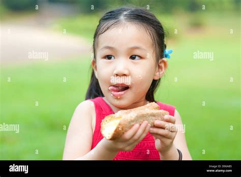 Little Asian Girl Eats A Sandwich And Licking Lips On Fresh Air Stock