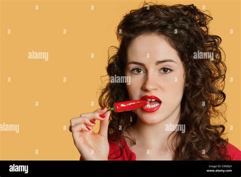 Portrait Of A Young Woman Biting Red Chili Pepper Over Colored