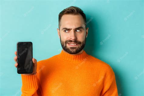 Premium Photo Confused Guy Scartching Head And Showing Smartphone