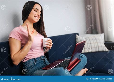 Cheerful Young Woman Sit On Sofa And Wave With Hand She Smiles And Look On Laptop Screen Model