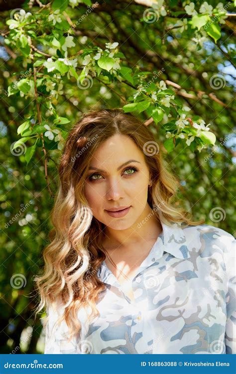 Portrait Of A Beautiful Blonde Girl With Green Eyes And Blossoming Apple Tree With White Flower