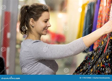 A Young Woman Chooses A Dress In A Fashionable Clothing Boutique