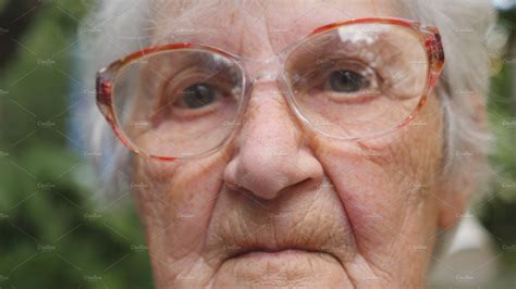 Old Woman In Glasses Looking Into Camera Outdoor Portrait Of Sad