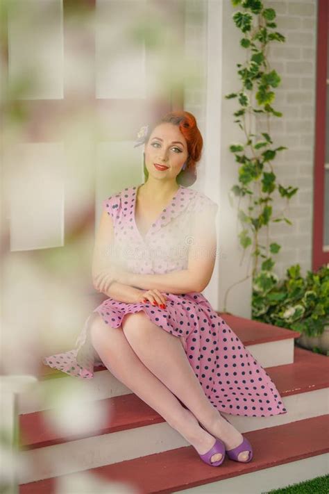 Beautiful Redheaded Pin Up Girl In Pink Polka Dot Dress And Vintage Stockings Posing Near The