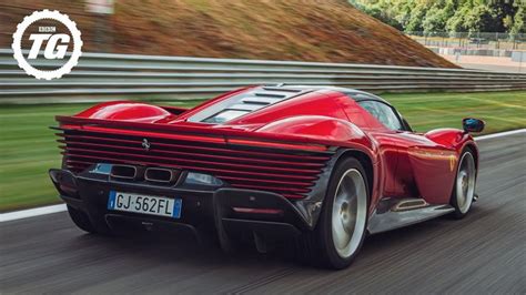 A Red Sports Car Driving Down A Road Next To A Green Grass Covered Hill