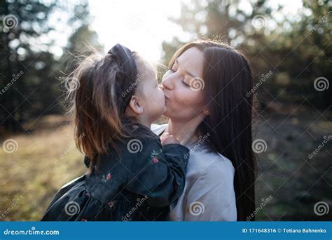 Close Up Portrait Of Beautiful Dark Haired Mom Kisses Into Lips Her Daughter On The Forest