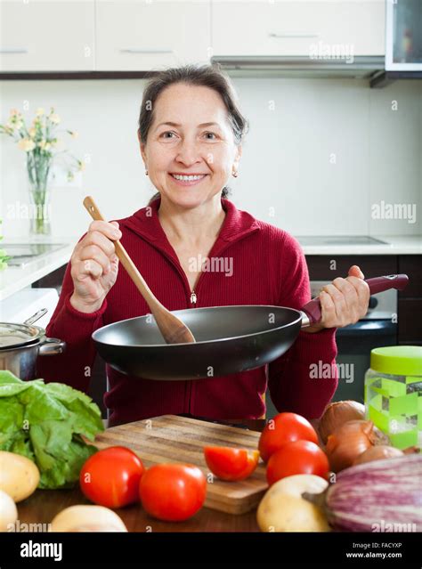 Smiling Mature Woman Cooking With Skillet In Domestic Kitchen Stock