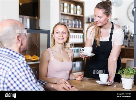 vigorous waiter girl brought cup of coffee for couple of different aged people in a cafe stock