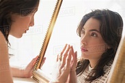 Serious young woman looking into mirror - Stock Photo - Dissolve