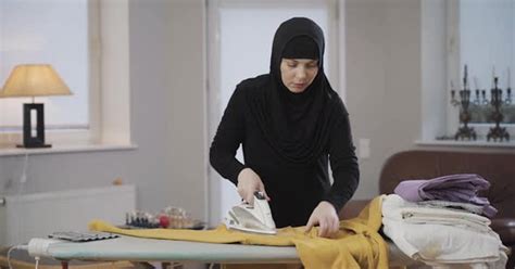 Portrait Of Concentrated Muslim Woman In Hijab Ironing Yellow Pullover