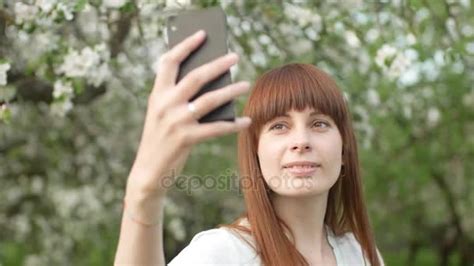 happy asian girl taking a selfie with a daisy between her hair and daisies covered garden