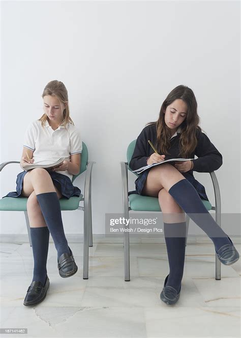 Two Girls Wearing Uniforms Sit On Chairs Doing School Work Photo