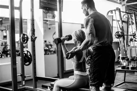 sporty girl doing weight exercises with assistance of her personal trainer at gym stock image